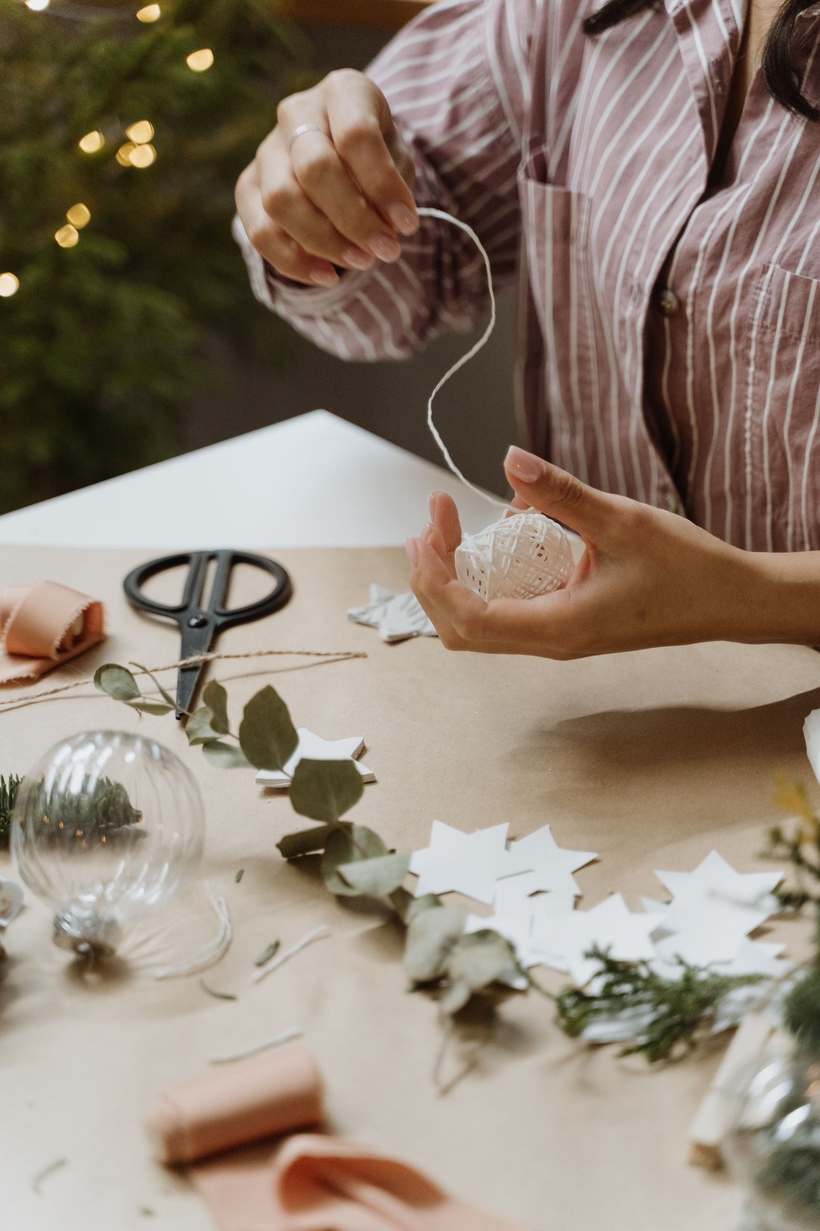 Handmade paper star Christmas ornaments and greenery being prepared with string