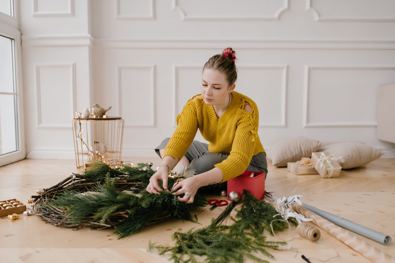 Woman sitting on the floor decorating a homemade Christmas wreath in a cosy room